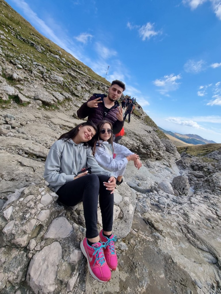 Three hikers resting on pale rock on an open Carpathian ridge trail under a clear sky