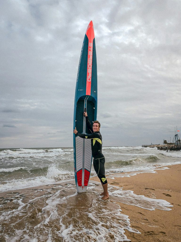 Guy holding a large Surfboard on a beach