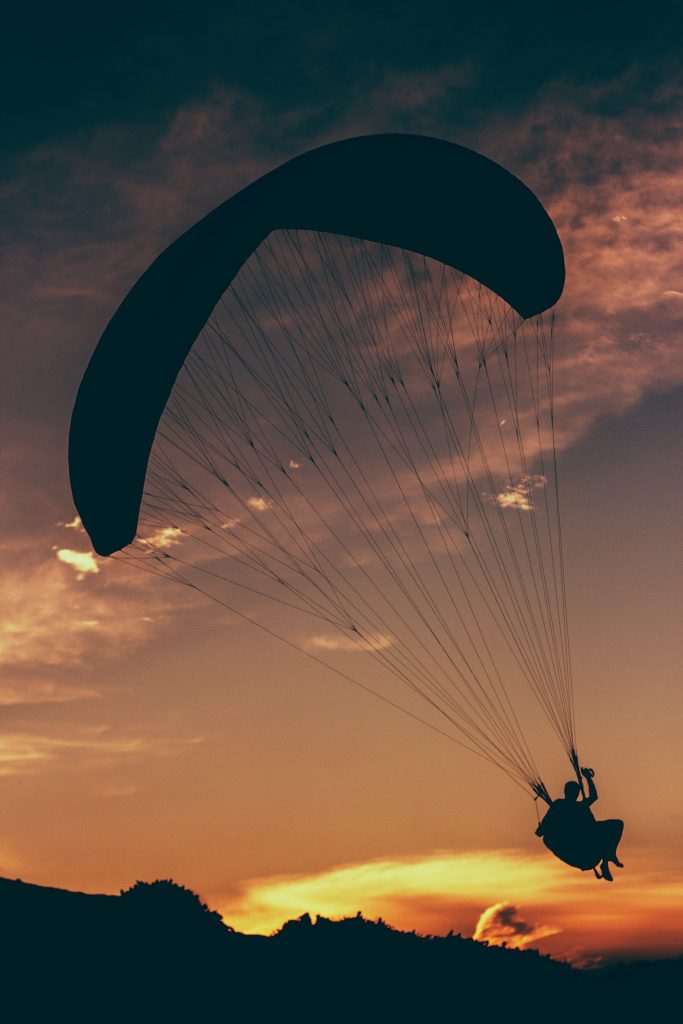 Paraglider flying over a hill in the sunset